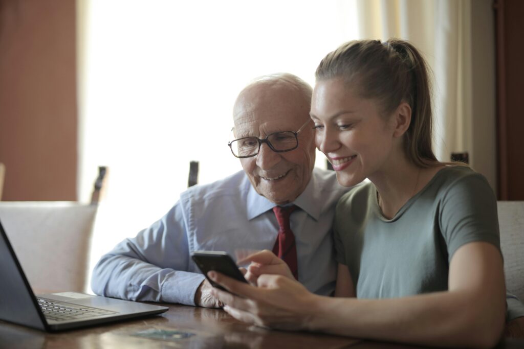 lachende jonge vrouw die een oudere man helpt zij iphone bankieren app beter te gebruiken om veilig te internetten