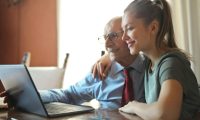 pexels-photo-3823489-3823489 Elderly man and young woman bonding while using a laptop indoors.
